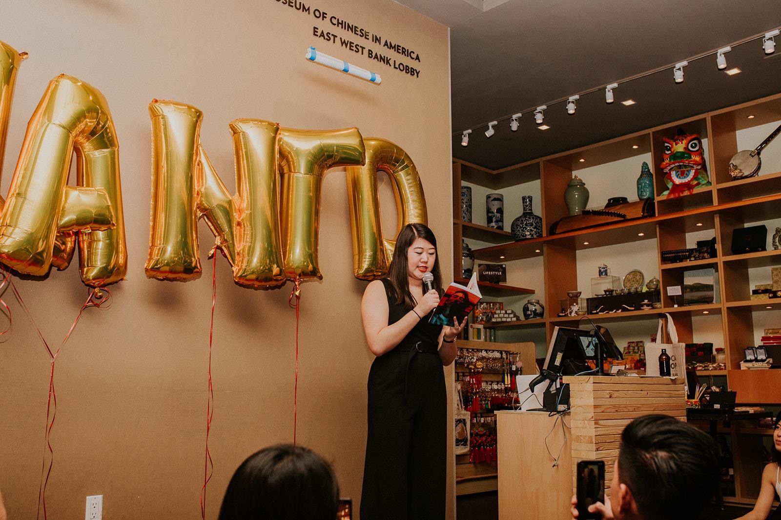 The author in a black jumpsuit reading her essay from Slant'd Issue 02 at the Museum of Chinese in America